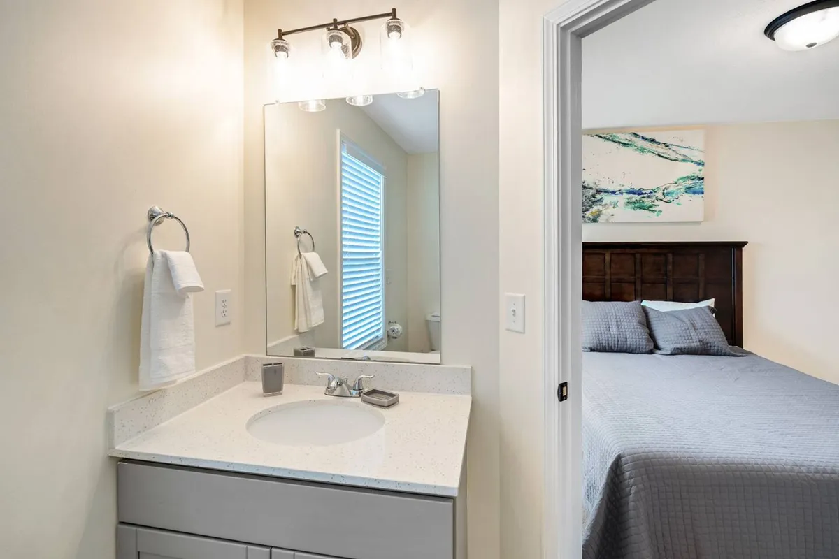 A bright vanity area with a large mirror and sink, offering a glimpse of the bedroom through the doorway. The setup evokes a sense of morning refreshment and personal relaxation, setting the stage for a day of exploration or winding down at night.