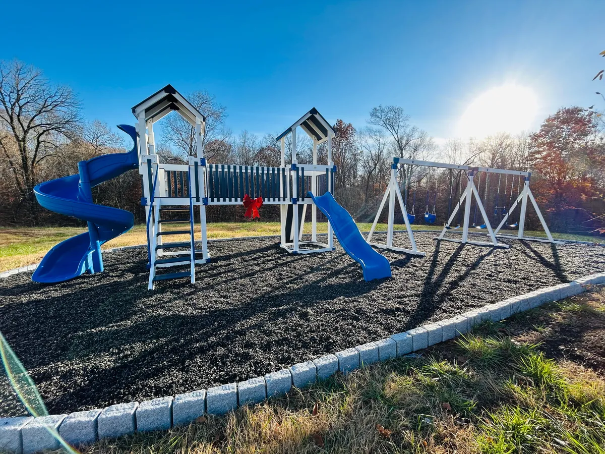 A vibrant playground with blue slides and a swingset sits in a lush, open area. Children can be seen playing and families gather for picnics, evoking a joyful, active environment perfect for young families.